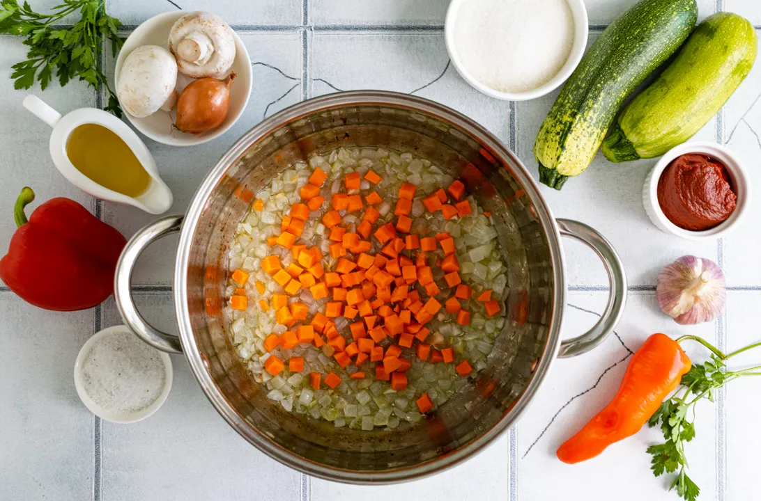 Wash the carrots, peel them, and cut them into medium-sized cubes. Add the carrots to the pot with the onion.