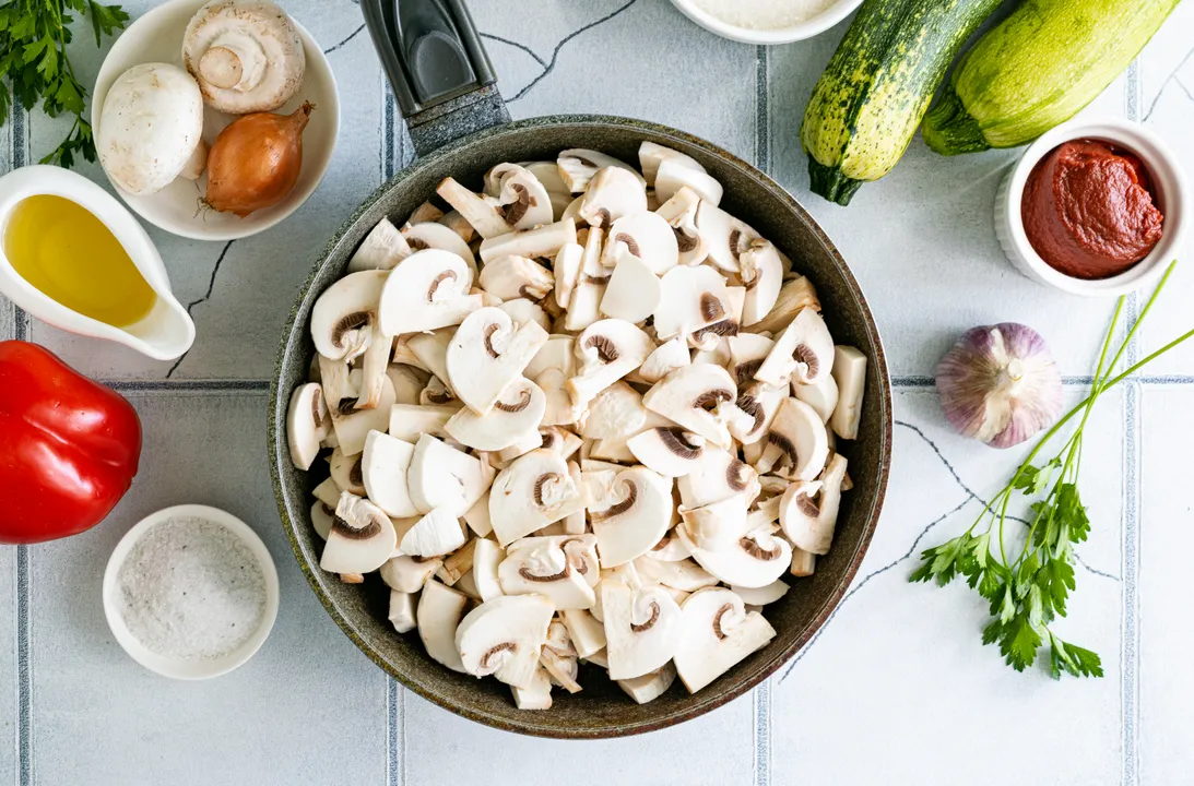 Meanwhile, wash the fresh mushrooms, and if necessary, clean the mushroom caps with a knife. Cut the mushrooms in half, slice them 3-4 mm thick, and place them in a pan.