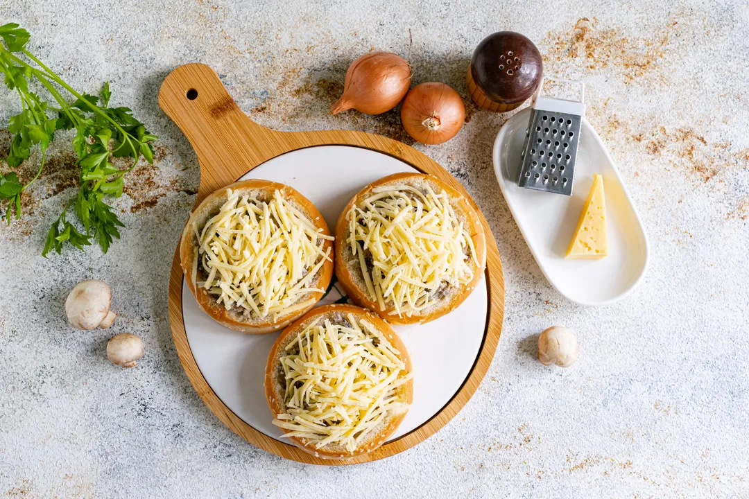 A kemény sajtot reszelje le nagy lyukú reszelőn, majd egyenletesen ossza el a gombás zsemlék tetején.