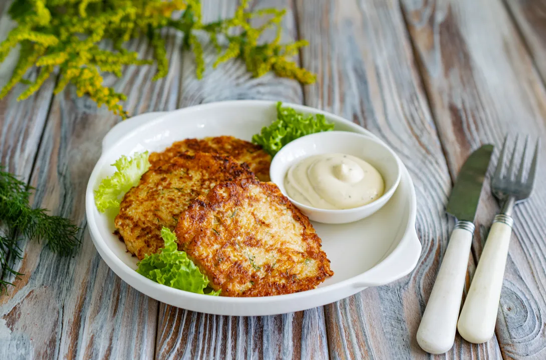 Подавай оладки гарячими чи теплими, поки розплавлений твердий сир залишається тягучим усередині. Страву можна доповнити ложкою сметани, натуральним йогуртом, пряним соусом на основі часнику та зелені або легкою вершковою заправкою.