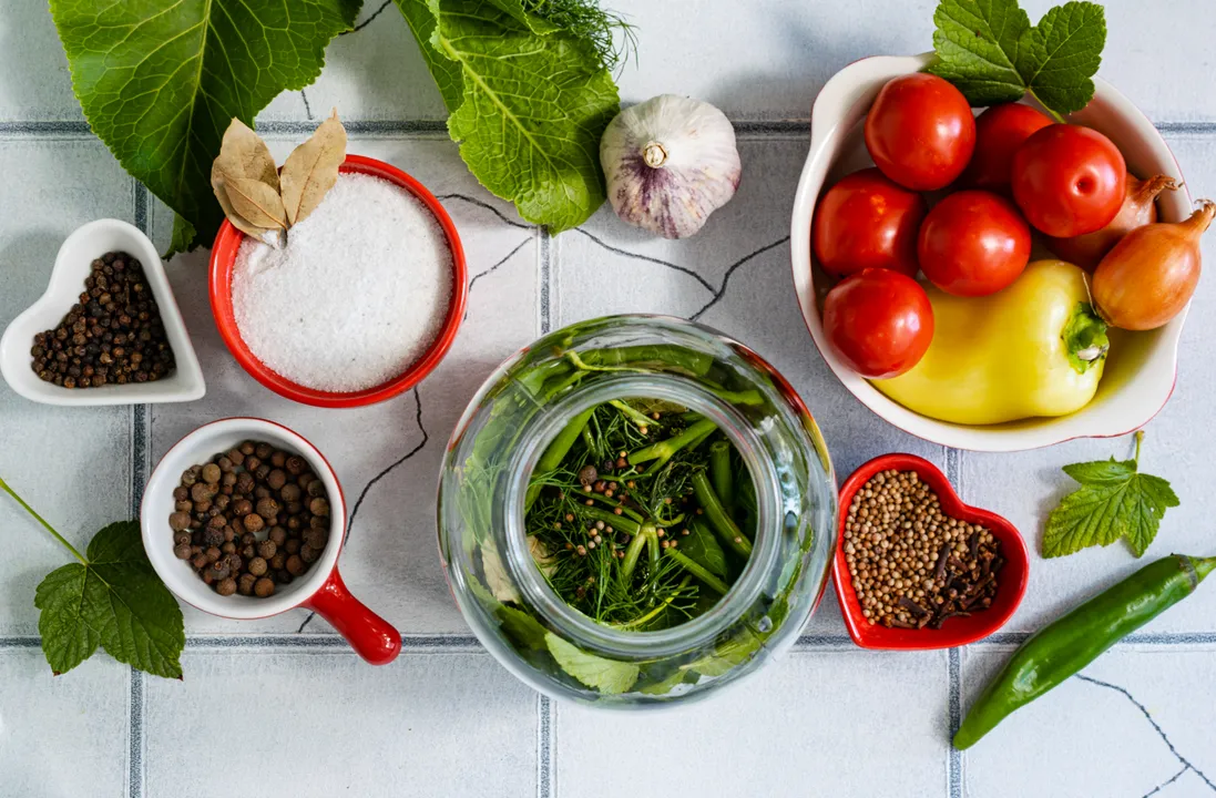 Sterilize glass jars for preservation using steam, an oven, or a microwave. At the bottom of each jar, place dill umbrellas and sprigs, horseradish leaves, blackcurrant, apple, cherry, and bay leaves. Add 0.5 teaspoon of a pepper and coriander seed mixture to each jar. Put in 3 peppercorns of allspice and 1 clove bud.