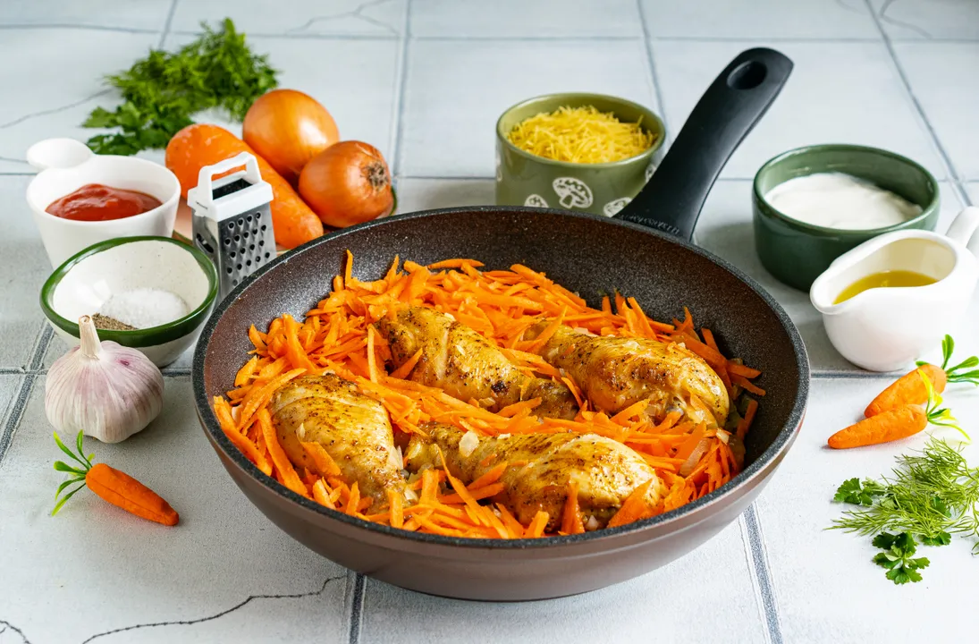 Моркву помийте, очистьте від шкірки, подрібніть на тертці з великим полотном. Додайте моркву в сковороду з куркою та цибулею.